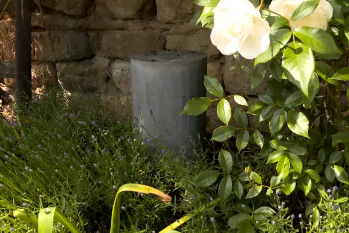 Zylinderförmiger Lautsprecher aus Beton zwischen Lavendel und Rosen